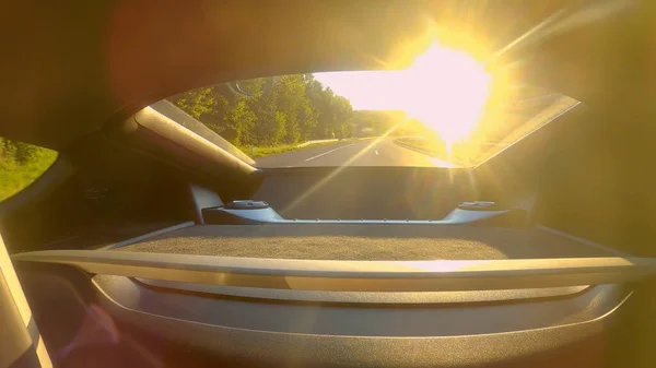 CERRAR: rayos de sol dorados brillan a través de la ventana trasera del coche que conduce por la carretera. — Foto de Stock