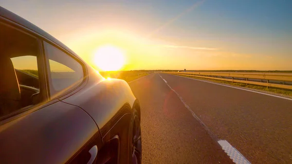 CHIUSURA: Sunrise illumina la sportscar nera percorrendo un'autostrada. — Foto Stock