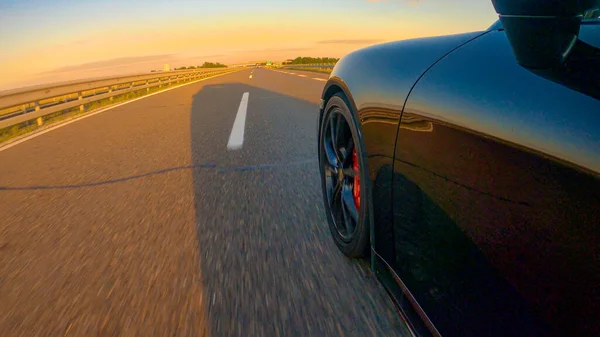 CERRAR: Fotografía cinematográfica de un Porsche negro conduciendo por una carretera vacía. — Foto de Stock