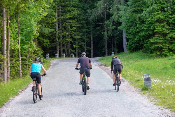 Három felismerhetetlen turista biciklizik fel egy üres aszfaltozott úton Kranjska Gora közelében. — Stock Fotó
