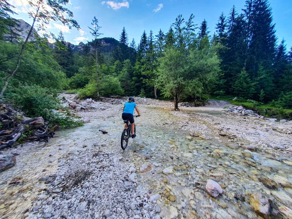 Felismerhetetlen nő a hegyi kerékpártúrán keresztezi a kristálytiszta patakot. — Stock Fotó