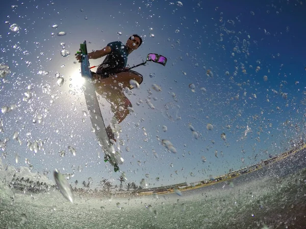 ÁNGULO BAJO: Joven atlético salpica agua en la cámara mientras practica kitesurf. —  Fotos de Stock