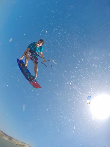 VERTICAL: Maschio kitesurfer spruzza acqua alla fotocamera mentre fa un trucco. — Foto Stock