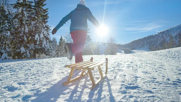 低角度：无法辨认的年轻女子拉着雪橇沿着雪地的草地奔跑 — 图库照片
