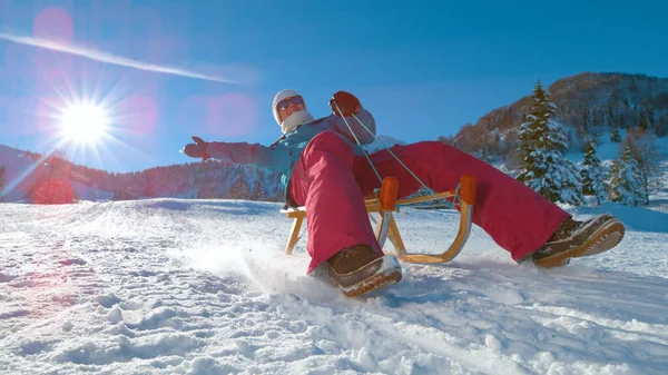 FLARE DE LA LENTE: Feliz mujer caucásica acelera por la colina nevada en un trineo de madera. — Foto de Stock