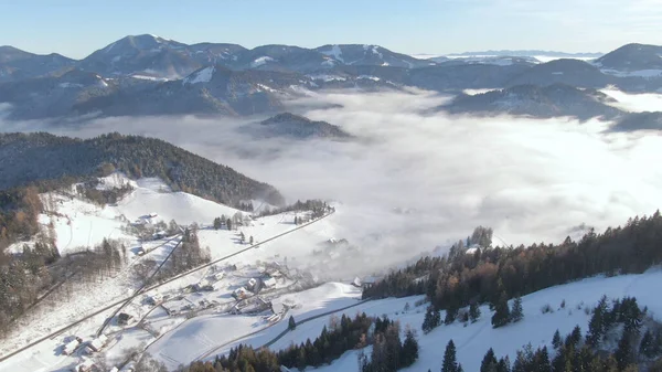 AERIAL: Klein dorpje in de serene Juliaanse Alpen op een mistige winterochtend. — Stockfoto