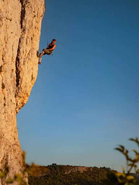 VERTICAL: Fit young woman stops and looks back at sunset while rock climbing. — ストック写真