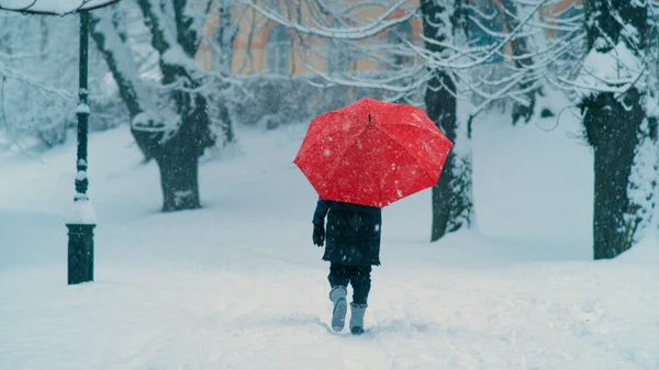 Kırmızı şemsiyeli tanınmayan bir kadın boş bir karlı caddede yürüyor.. — Stok fotoğraf