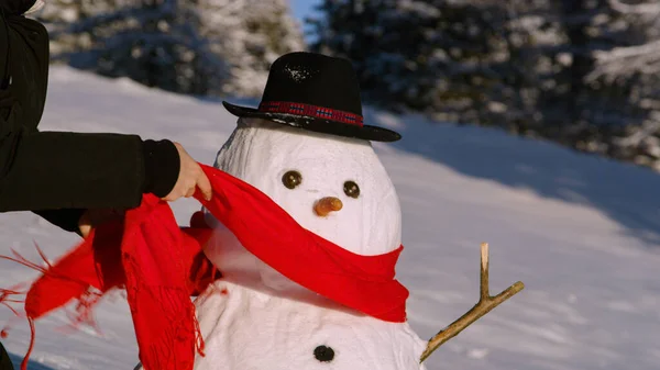 閉じる:雪の中で楽しんでいる若い女性は、雪だるまの首の周りにスカーフを置きます. — ストック写真