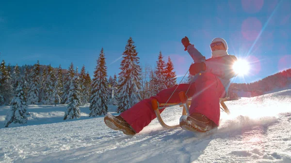 ÁNGULO BAJO: Mujer joven y feliz monta un trineo por una colina nevada en un día soleado. — Foto de Stock