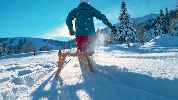 闭合：阳光灿烂的一天，一个难以辨认的女人拖着雪橇在厚厚的雪地里滑行. — 图库照片