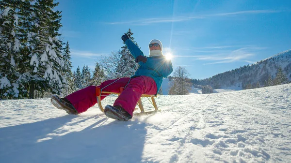 LOW ANGLE Woman outstretches her arm while sledding down snowy hill on sunny day — Stock Photo, Image