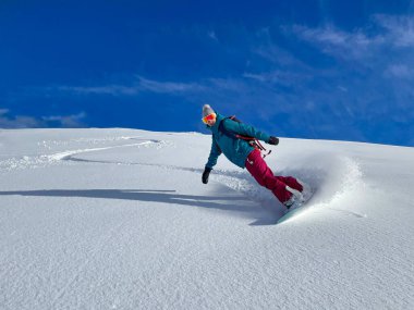 Gülümseyen genç bayan snowboardcu güneşli bir kış gününde bakımsız yamaçlara biner.