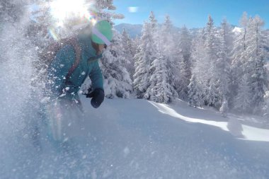 Tanınmayan kadın snowboardcu güneşli bir günde taze tozu parçaladı.