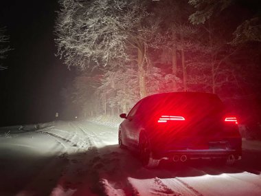 Metalik mavi araba, karlı kırsalda boş bir yolda ilerliyor..