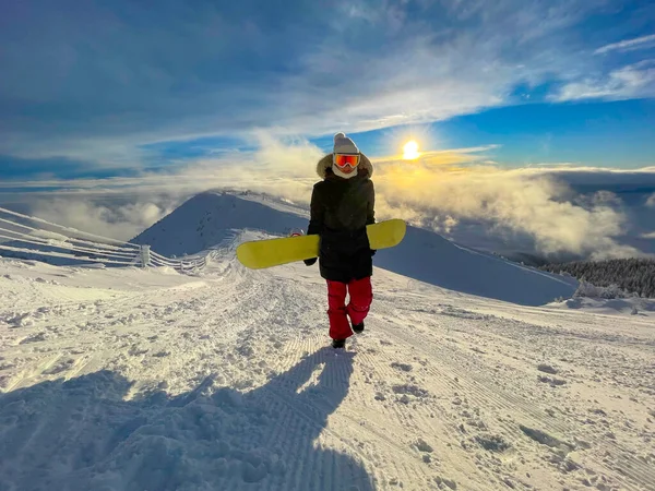 PORTRAIT: Cheerful woman snowboarding at a closed ski resort hikes up a slope. — Stock Photo, Image