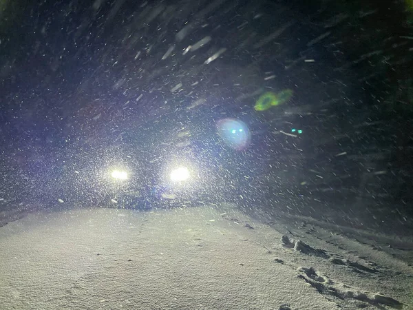 Faróis LED brilhantes de sportscar ilumina a estrada nevada em uma noite de inverno. — Fotografia de Stock