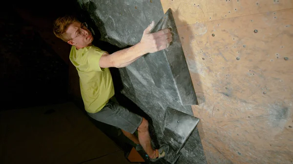 CLOSE UP, DOF: Focused male climber grips a black volume hold while training.