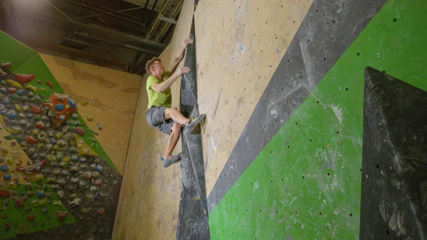 ÁNGULO BAJO: El hombre atlético sube por una ruta de escalada difícil en el gimnasio de bouldering. —  Fotos de Stock