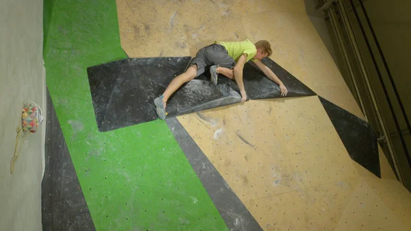 VERTICAL : Jeune homme grimpe mur artificiel en utilisant uniquement des prises de volume noir. — Photo