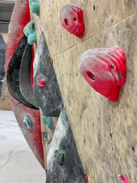 VERTICALE Le prese per brocche rosse e turchesi sono sparse su una parete da arrampicata — Foto Stock