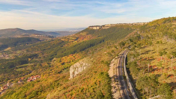 DRONE: Bahngleise verlaufen entlang eines Hügels mit Blick auf das fallfarbene Tal bei Crni Kal — Stockfoto