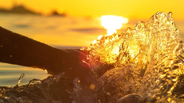 CHIUDI: Giovane donna spruzza acqua trascinando la mano lungo la superficie del mare. — Foto Stock