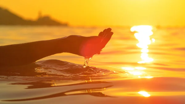 CERRAR: Atardecer de oro brilla en la mano de la mujer ventosa un puñado de agua de mar. — Foto de Stock