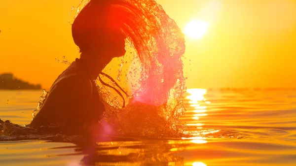 LENS FLARE: Veduta panoramica di una giovane donna che spruzza l'acqua dell'oceano con i capelli. — Foto Stock