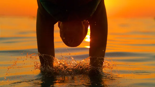 SILHOUETTE: Žena cestovatel skočí hlavou napřed do osvěžující mořské vody. — Stock fotografie