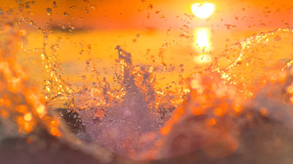 LENS FLARE: A splash of ocean water rushes towards the camera filming sunset. — ストック写真