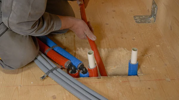 CHIUSURA: L'idraulico irriconoscibile spinge i tubi nel pavimento in legno duro. — Foto Stock