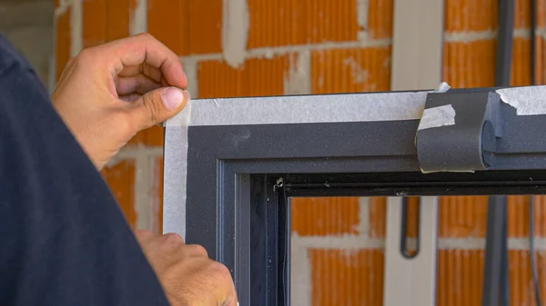 CHIUSURA: Handyman utilizza nastro adesivo bianco per proteggere il telaio della finestra nera. — Foto Stock