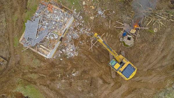 TOP DOWN: Excavator helps worker burn scraps while rebuilding an old farm. — ストック写真