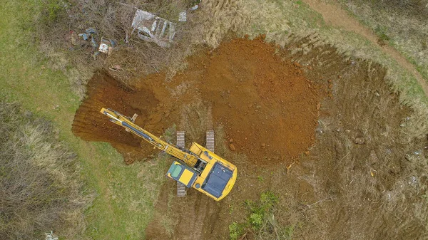 TOP DOWN: Drone point of view of yellow excavator digging a hole in countryside — ストック写真