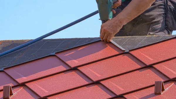 AFSLUITEN: Onherkenbare dakdekker legt aluminium tegels met behulp van een spijkerpistool Rechtenvrije Stockafbeeldingen