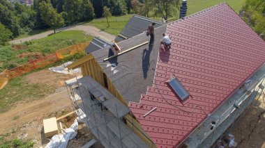 İşçiler inşaat halindeki modern bir eve kırmızı teneke çatı örtüleri seriyorlar.