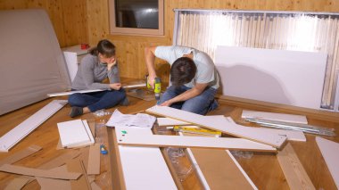 Genç çift yatak odasındaki mobilyaları monte etmek için birlikte çalışıyor..
