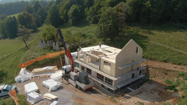 AERIAL: Truck boom lifts a massive CLT wall panel as workers assemble a house. — Stockfoto