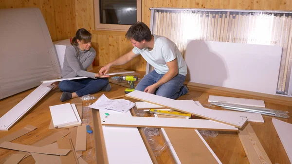 Genç çift yerde oturur ve yeni evlerinde bir yatak monte ederler.. — Stok fotoğraf
