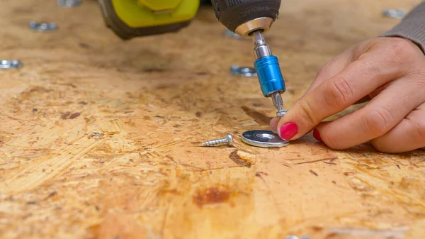 CERRAR: Mujer sujeta una lavadora de metal en una placa de madera contrachapada con un taladro de potencia. — Foto de Stock