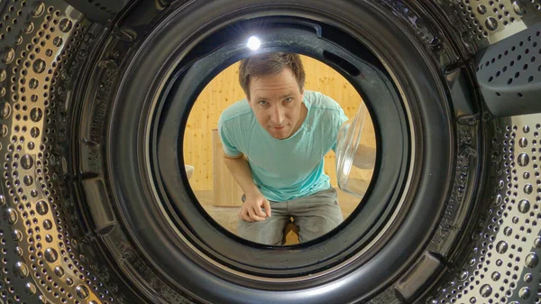 PORTRAIT: Smiling man opens the door and looks into the empty washing machine.