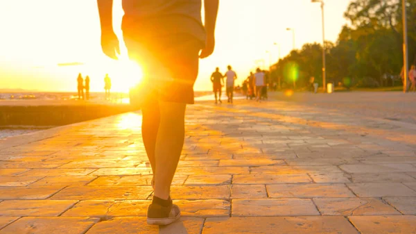 LOW ANGLE: Człowiek w szortach spaceruje po chorwackim promenadzie złotym światłem. — Zdjęcie stockowe