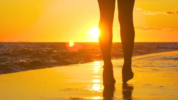 СИЛЬХУЭТТ: Женщина-туристка прогуливается вдоль берега на закате. — стоковое фото
