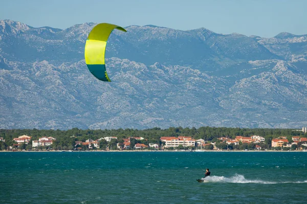 Hombre de vacaciones activas en Croacia kitesurfs más allá de una costa bajo el Velebit. — Foto de Stock