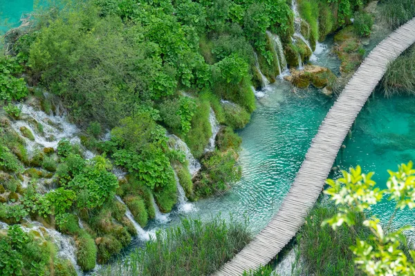 AERIAL: Vliegen boven promenade die over smaragdgroen meer en kleine watervallen loopt. — Stockfoto