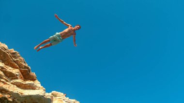 Atletik turist ferahlatıcı okyanusa dalmak için uçurumdan atlıyor..