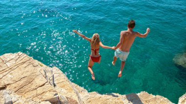 Tasasız genç turistler ferahlatıcı mavi denize atlarken el ele tutuşuyorlar..