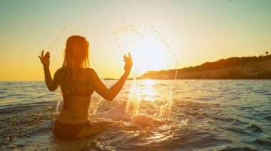 Sörfçü kız gün doğumunda sörf tahtasında oturur ve su sıçratır..