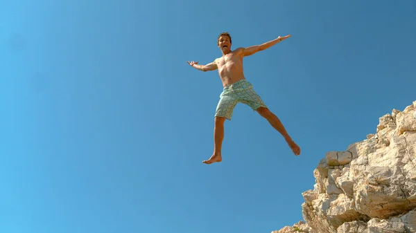 Excited male tourist jumps off edge of a cliff and outstretches arms and legs — Stockfoto